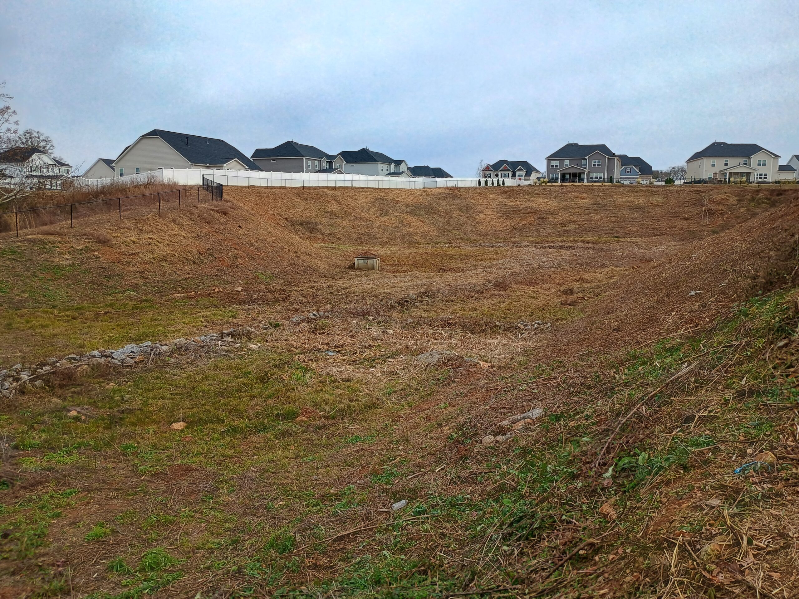Maintained retention pond in Simpsonville SC after mowing with clear slopes and visible basin near residential homes