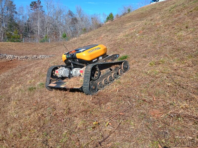 Remote-controlled slope mower cutting grass on a steep hillside in Greenville South Carolina